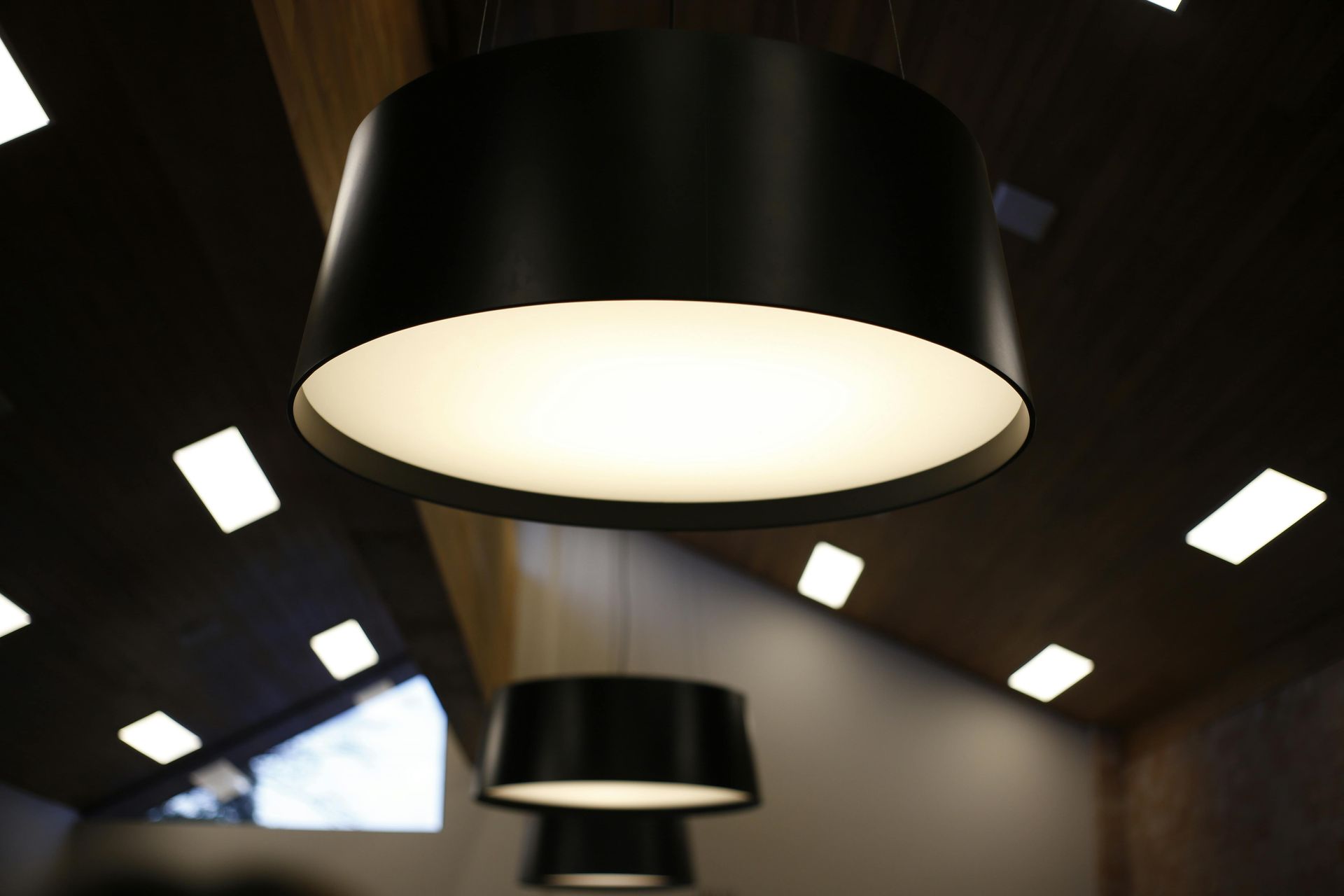 Black pendant lights with bright interior, set against a dark angled ceiling with recessed lights.