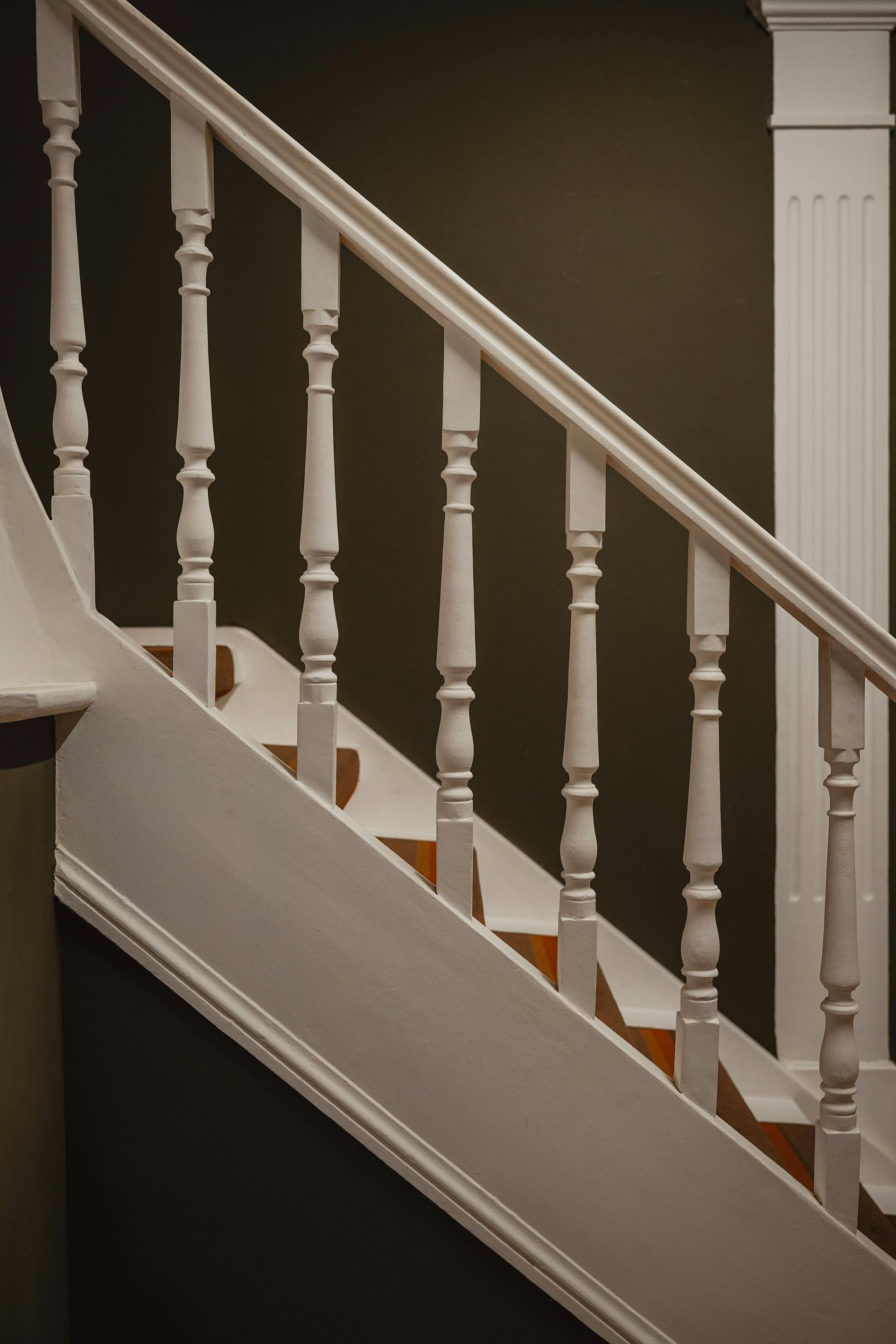White staircase with balusters and handrail against a dark green wall.