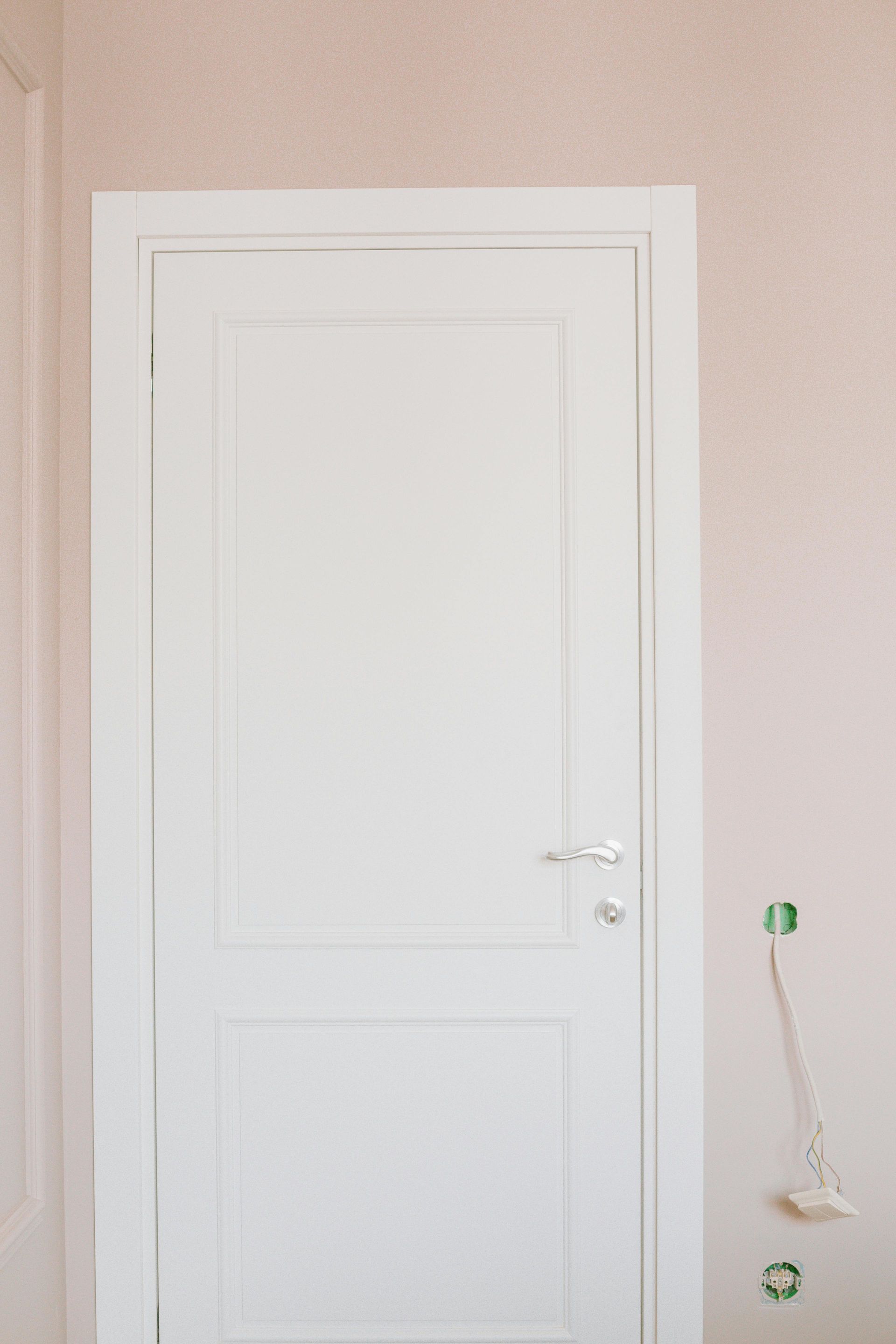 White door with silver handle and trim against a light pink wall.
