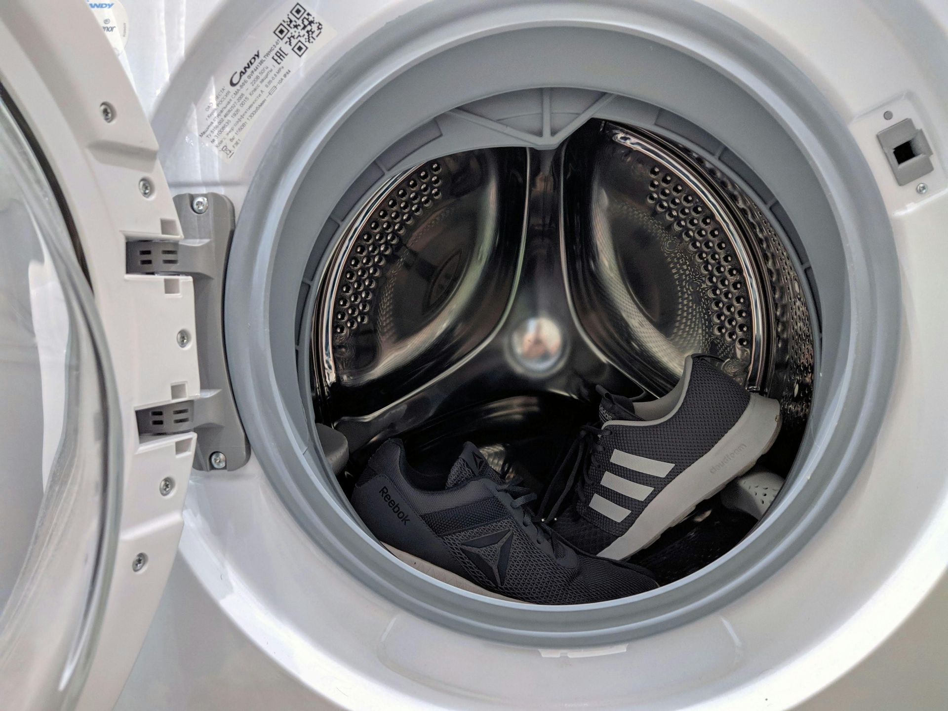 Inside a washing machine drum, two athletic shoes are being washed.