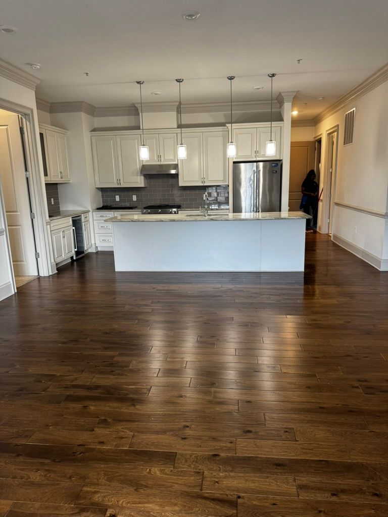 Open-concept kitchen with white cabinets, island, and stainless steel appliances. Hardwood floors and pendant lights.