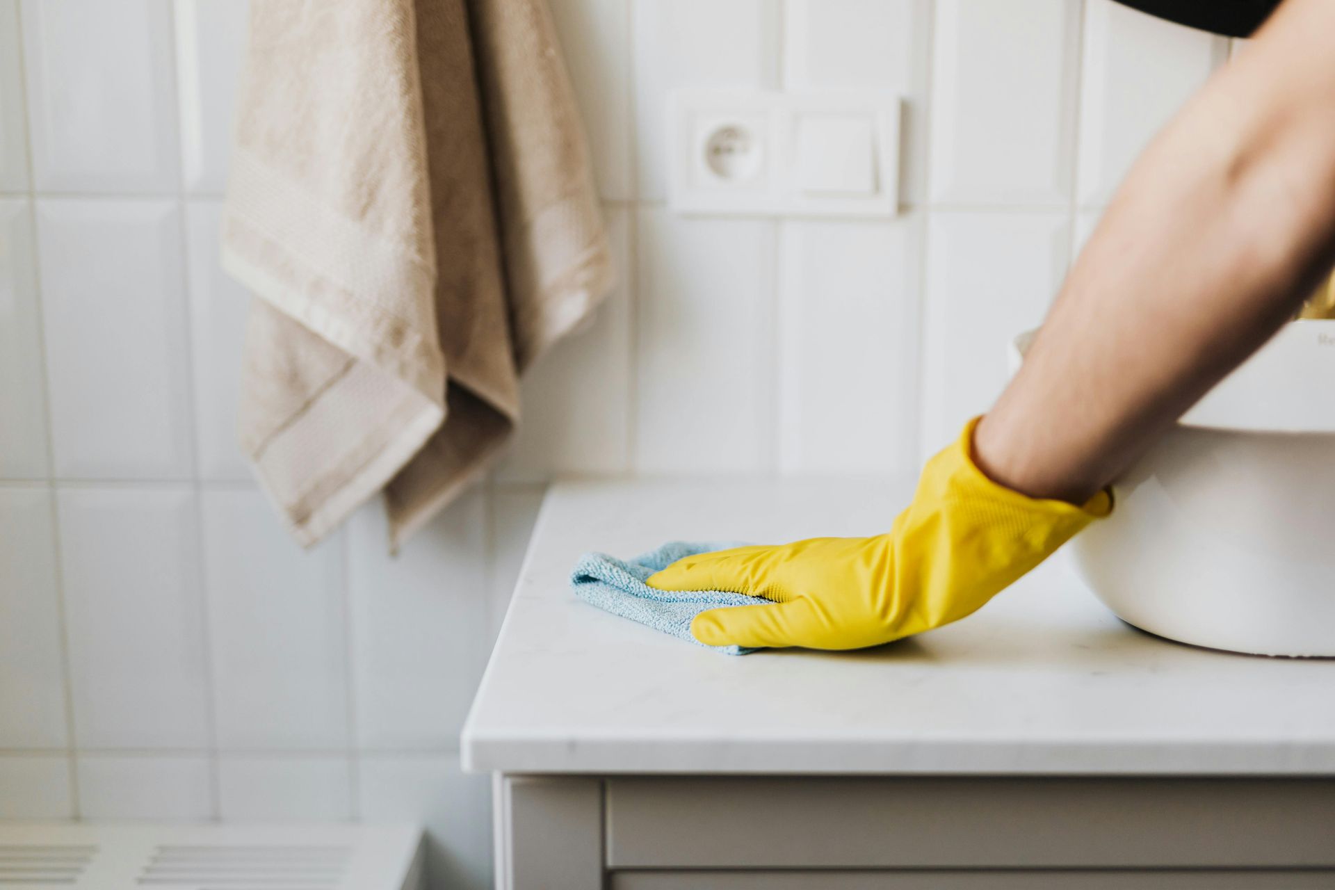 Person in yellow gloves cleaning a white bathroom vanity with a blue cloth.