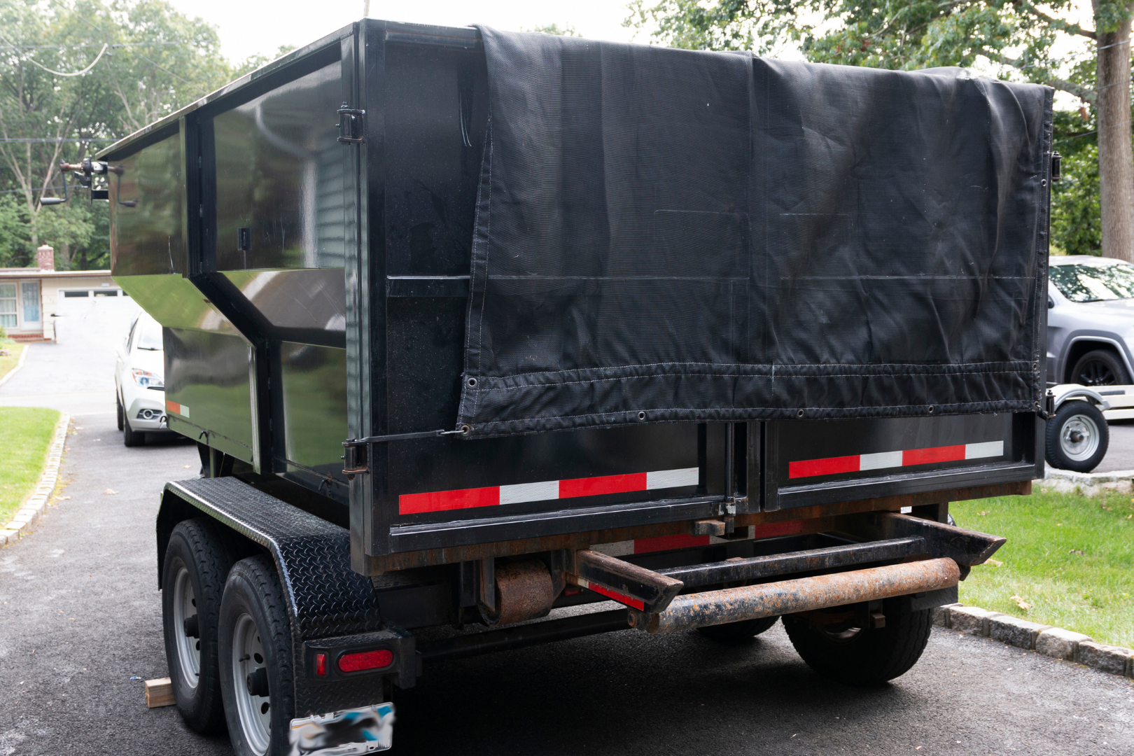 White utility trailer in a driveway in front of a garage, with a black front panel and hitch.