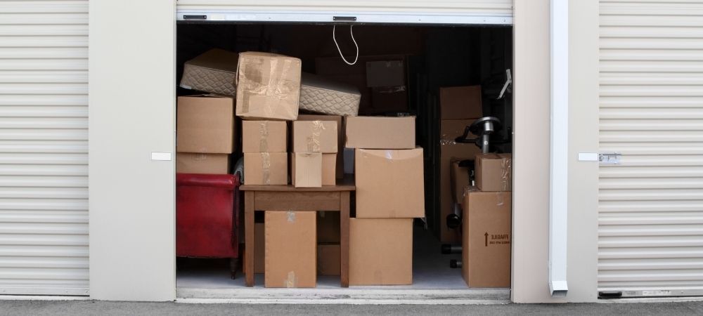 Storage unit filled with stacked cardboard boxes, seen through an open roll-up door