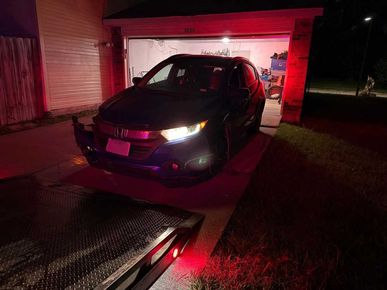 Black SUV backed onto a tow truck in front of a garage at night with red lights illuminating the scene.