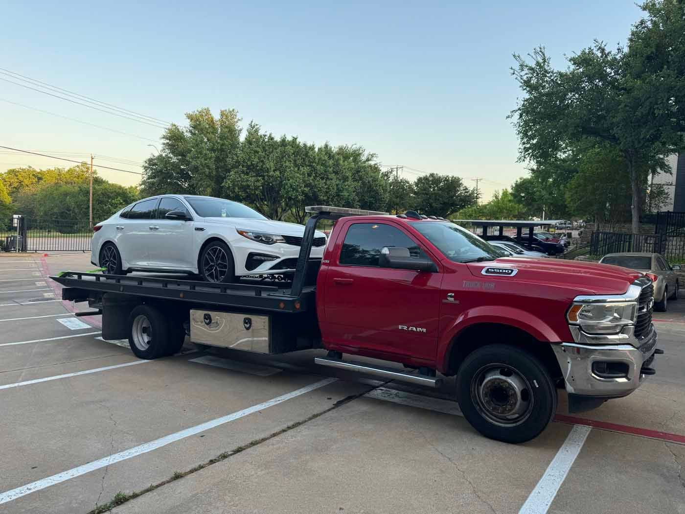 Red tow truck carrying a white sedan on a sunny day.