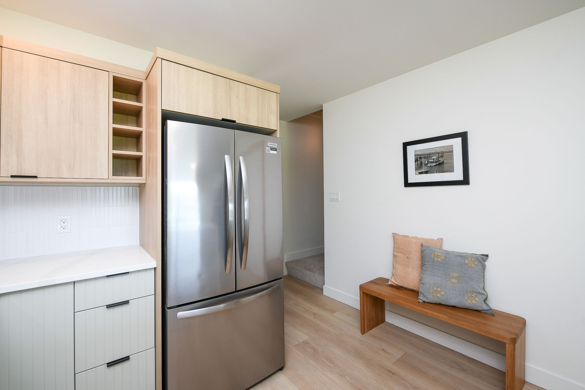 A kitchen with a stainless steel refrigerator and a wooden bench.