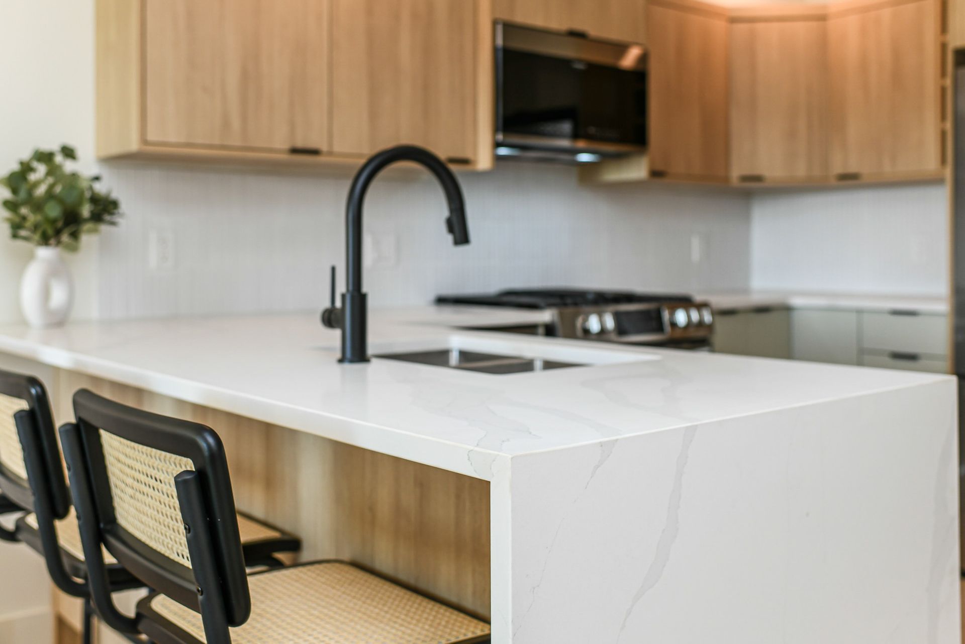 A kitchen with a white counter top , a sink , a stove , and a microwave.