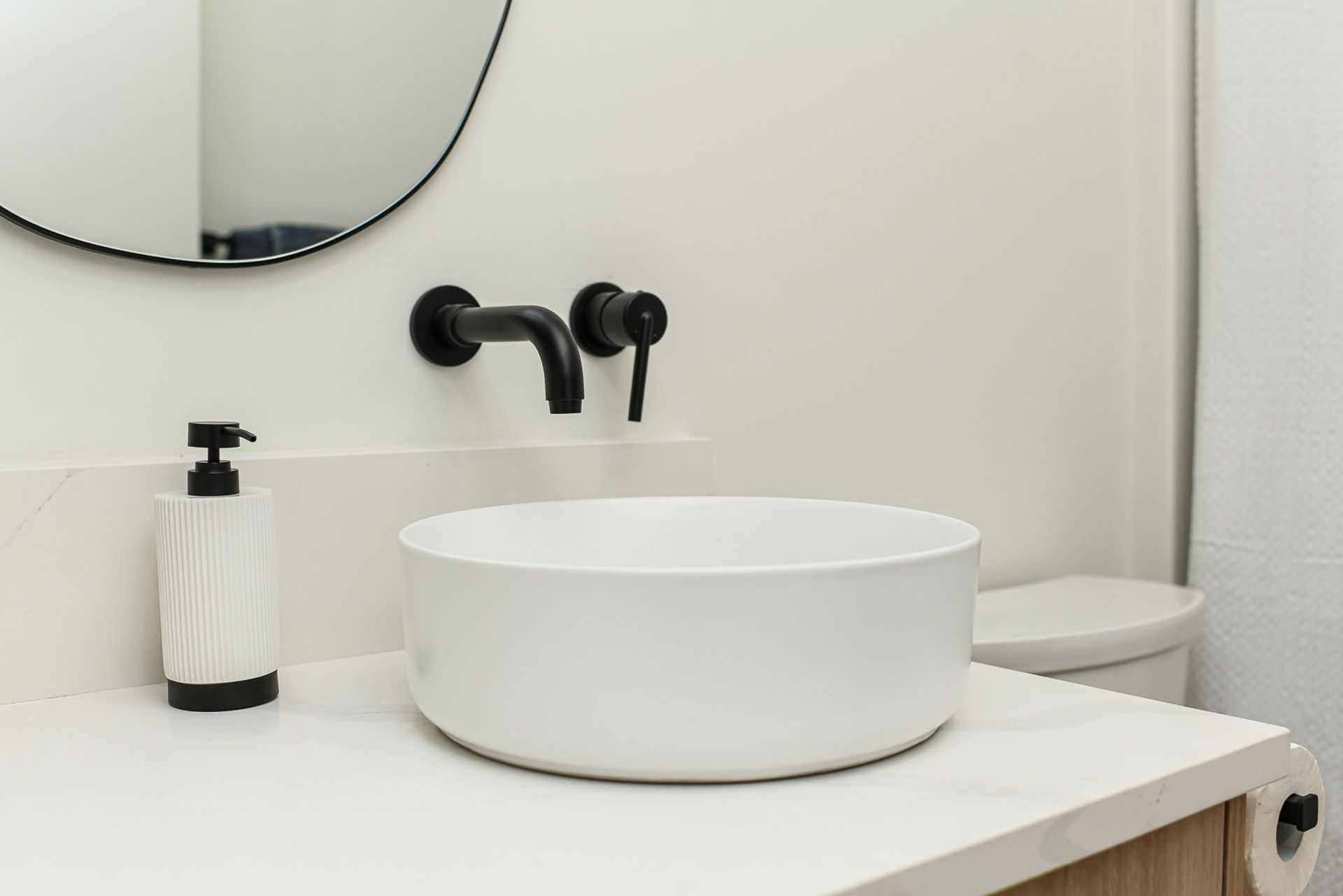 A bathroom with a sink , toilet , mirror and soap dispenser.