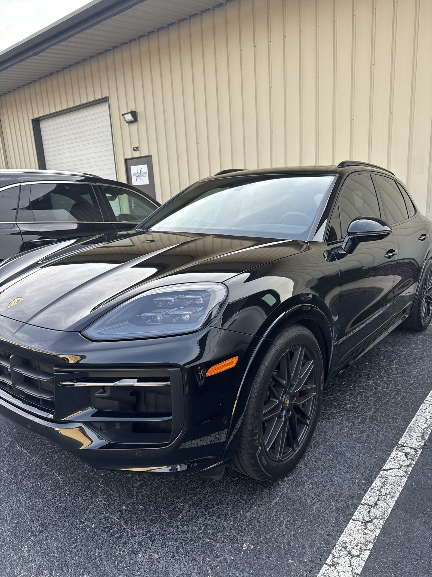 Black Porsche SUV parked in front of a building with a beige facade.