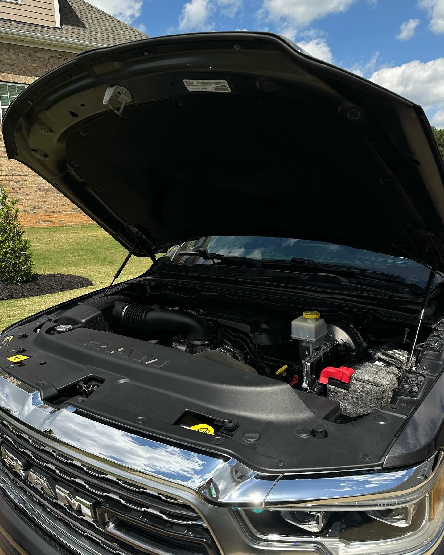 A truck with its hood open, revealing the engine bay. The truck is dark gray, and the setting is outdoors.