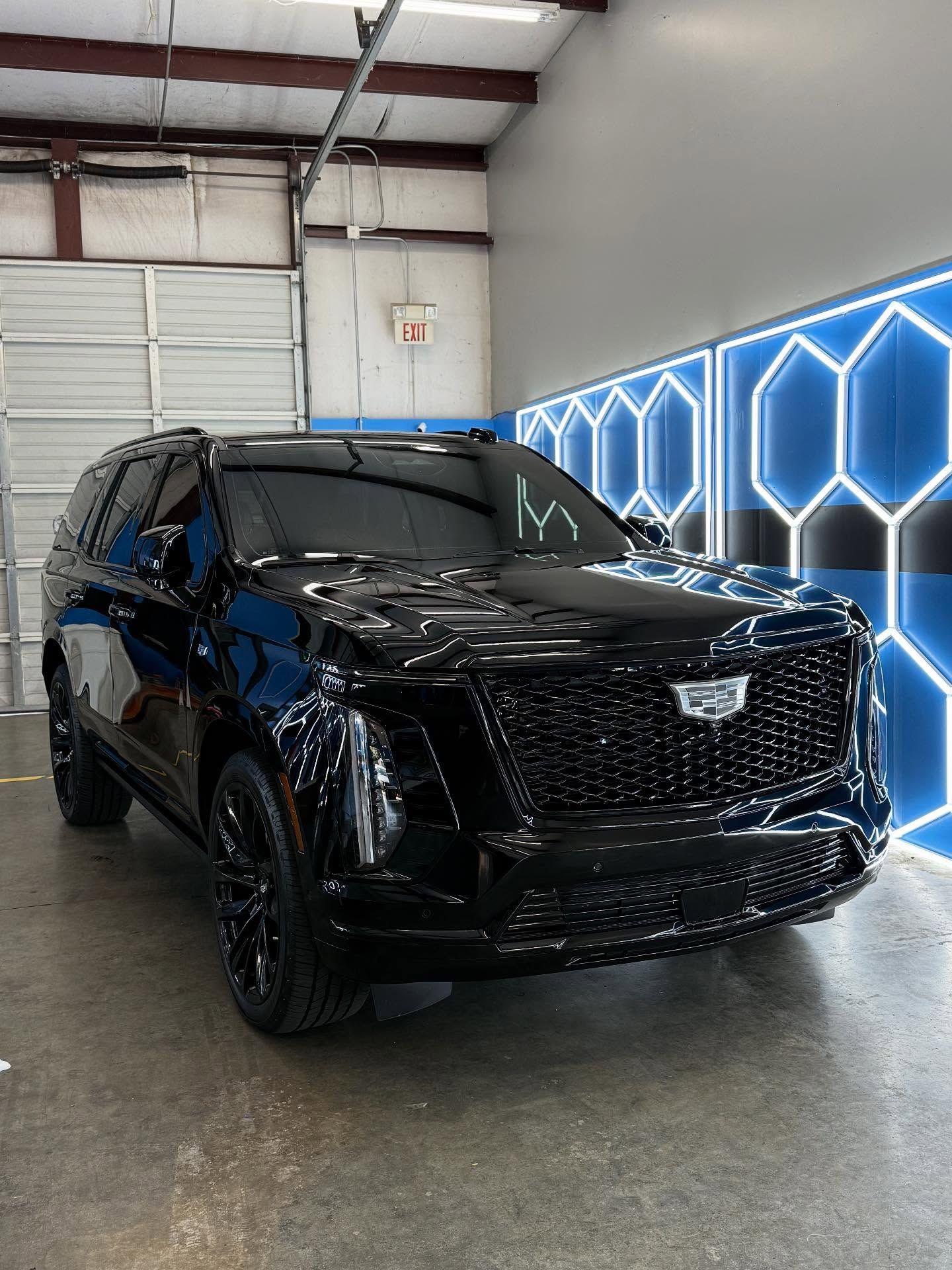 Black Cadillac Escalade SUV in a garage with neon blue honeycomb wall lights.