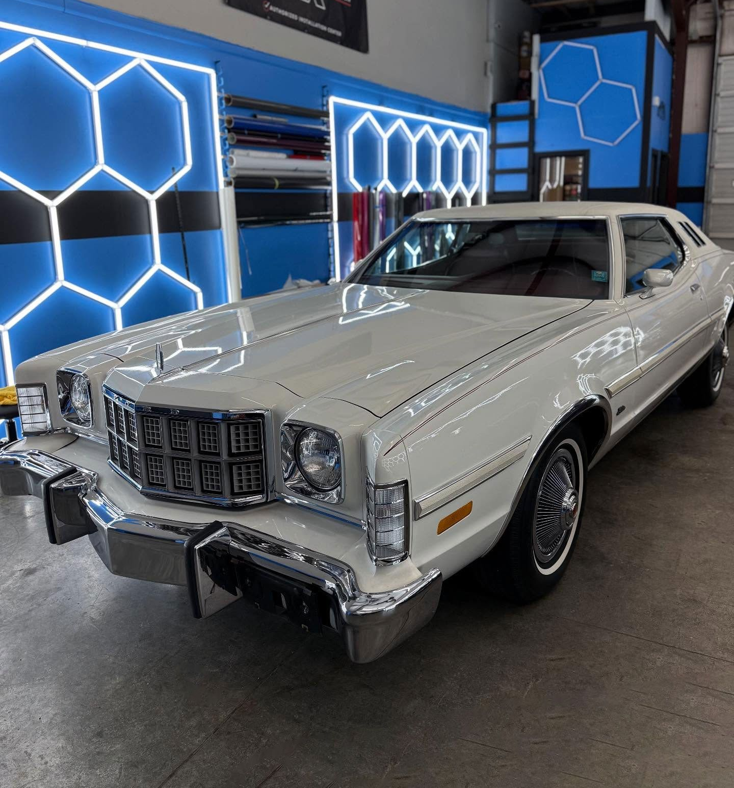 White 1970s Ford Torino car, chrome details, parked indoors with blue geometric neon lights.