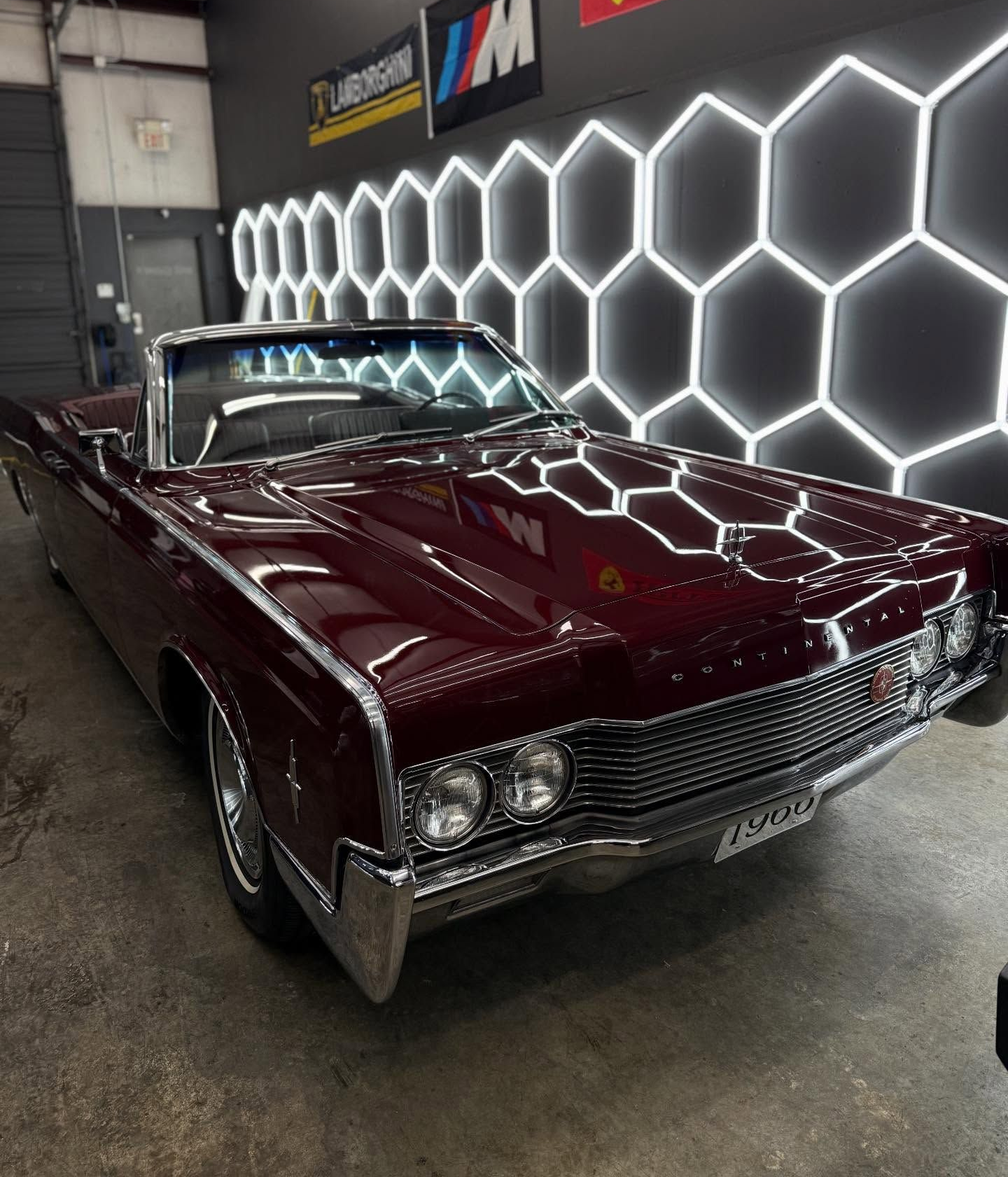 Classic burgundy convertible car in a garage with honeycomb lights.