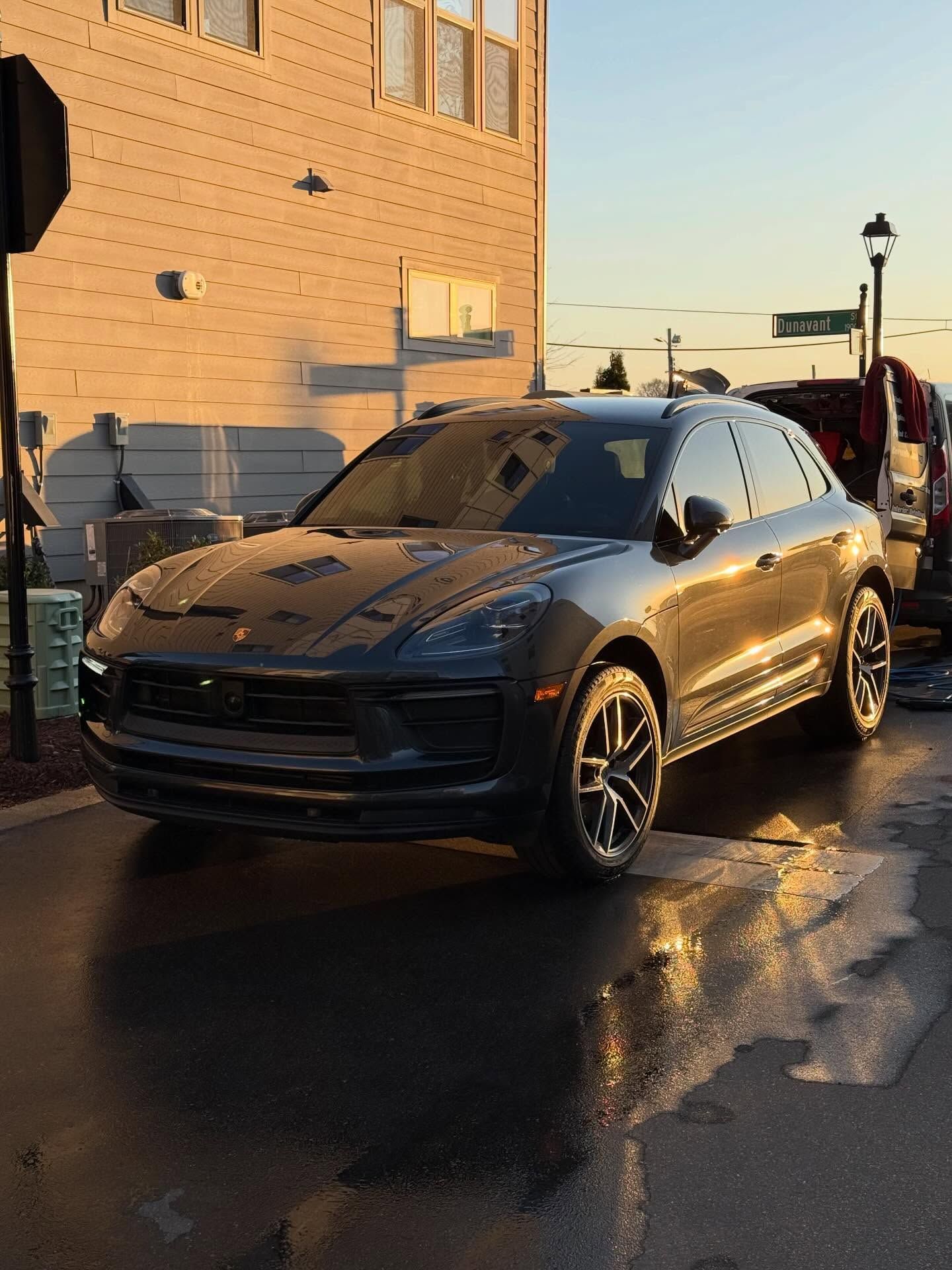 Gray Porsche Macan SUV parked on wet pavement; building in background.