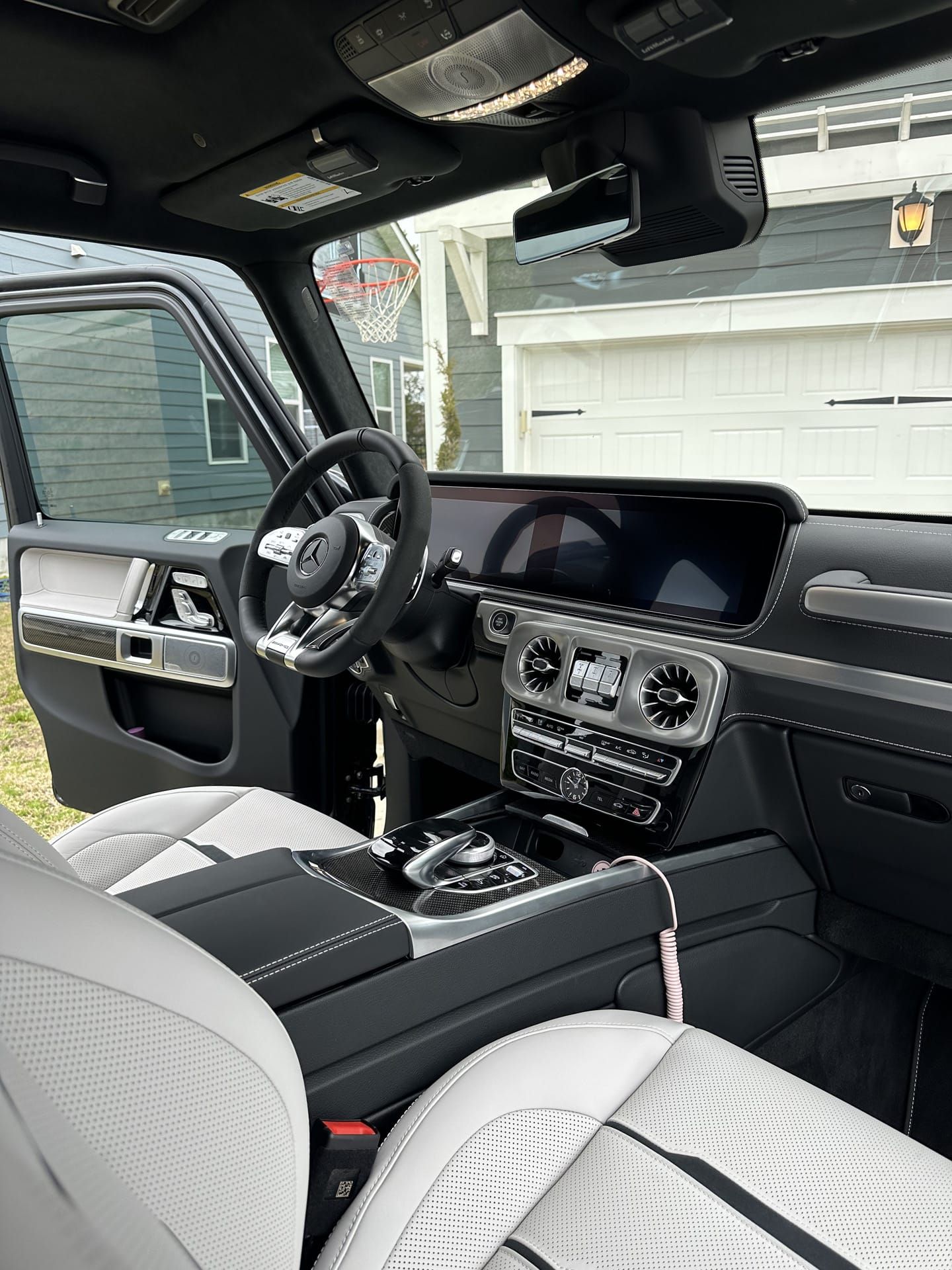 Interior of a luxury Mercedes-Benz G-Class SUV. Light-colored leather seats, black dashboard, and silver accents.