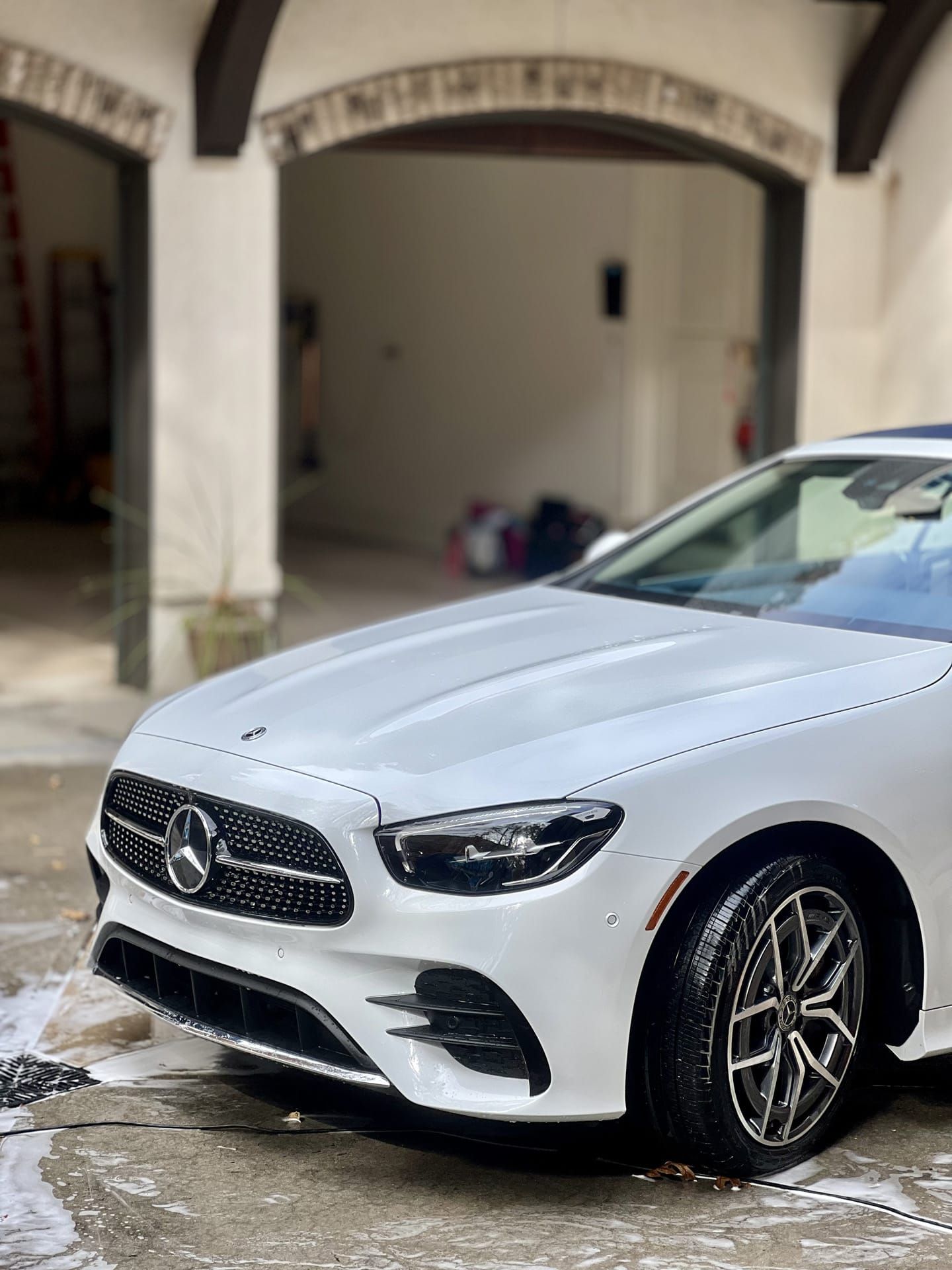 White Mercedes sedan being washed in a garage with an arched entryway.