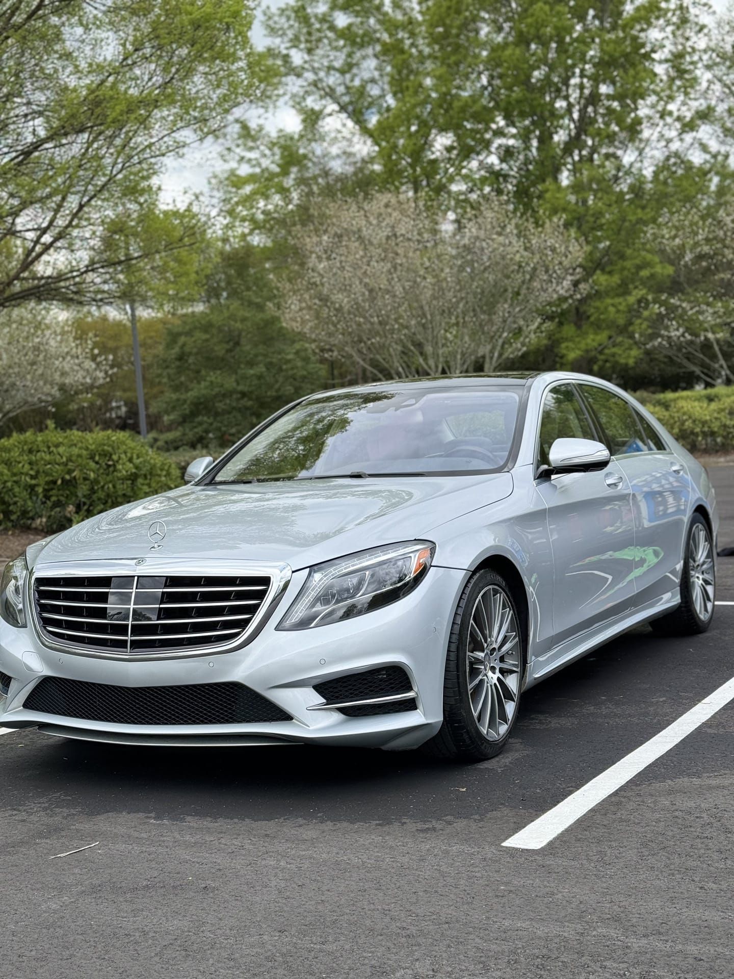 Silver Mercedes-Benz S-Class sedan parked in a parking spot with trees in the background.