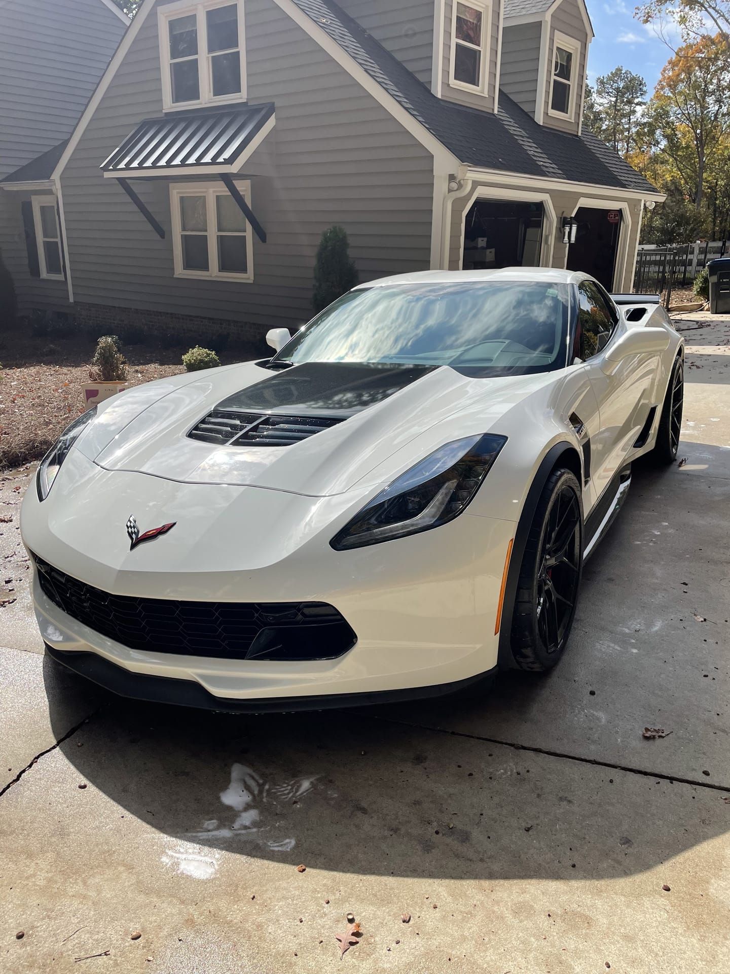 White sports car parked in front of a house. Black hood scoop, wheels, and trim.