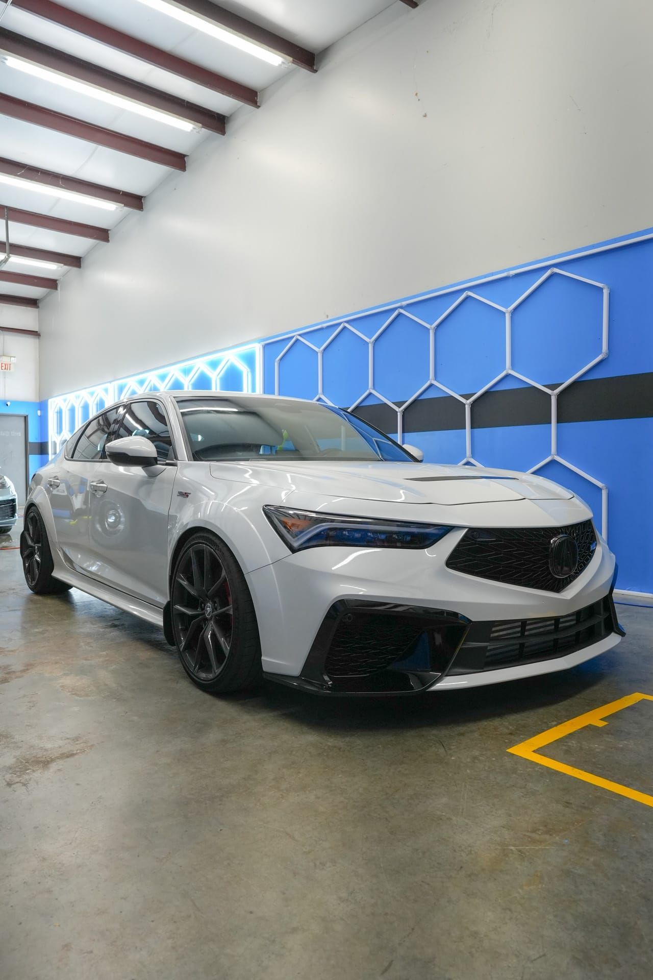 Gray Acura Integra in a car detailing bay, with black wheels and a blue hexagon wall.