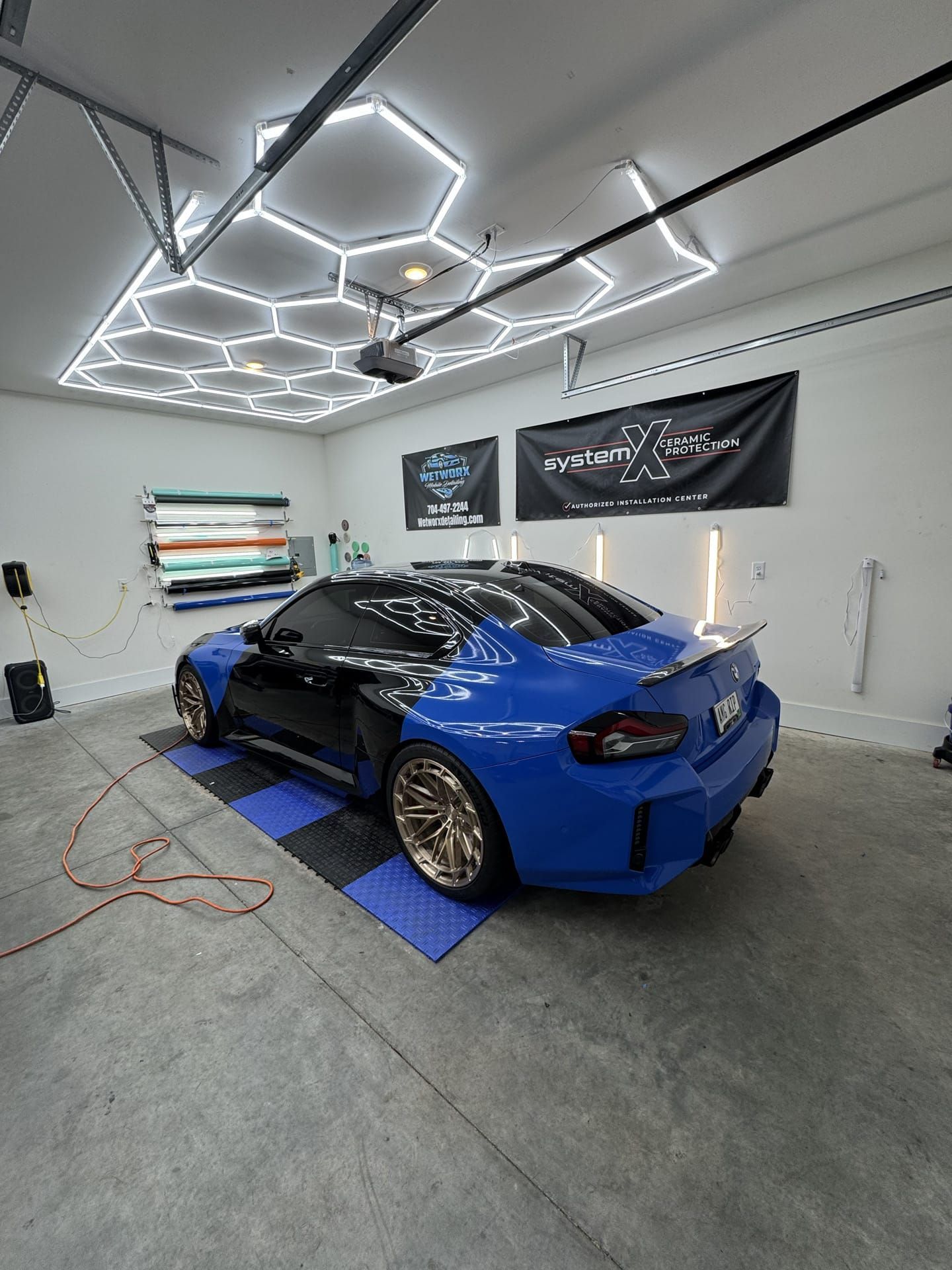 Blue and black car in a garage with honeycomb lights, on blue and black tile.