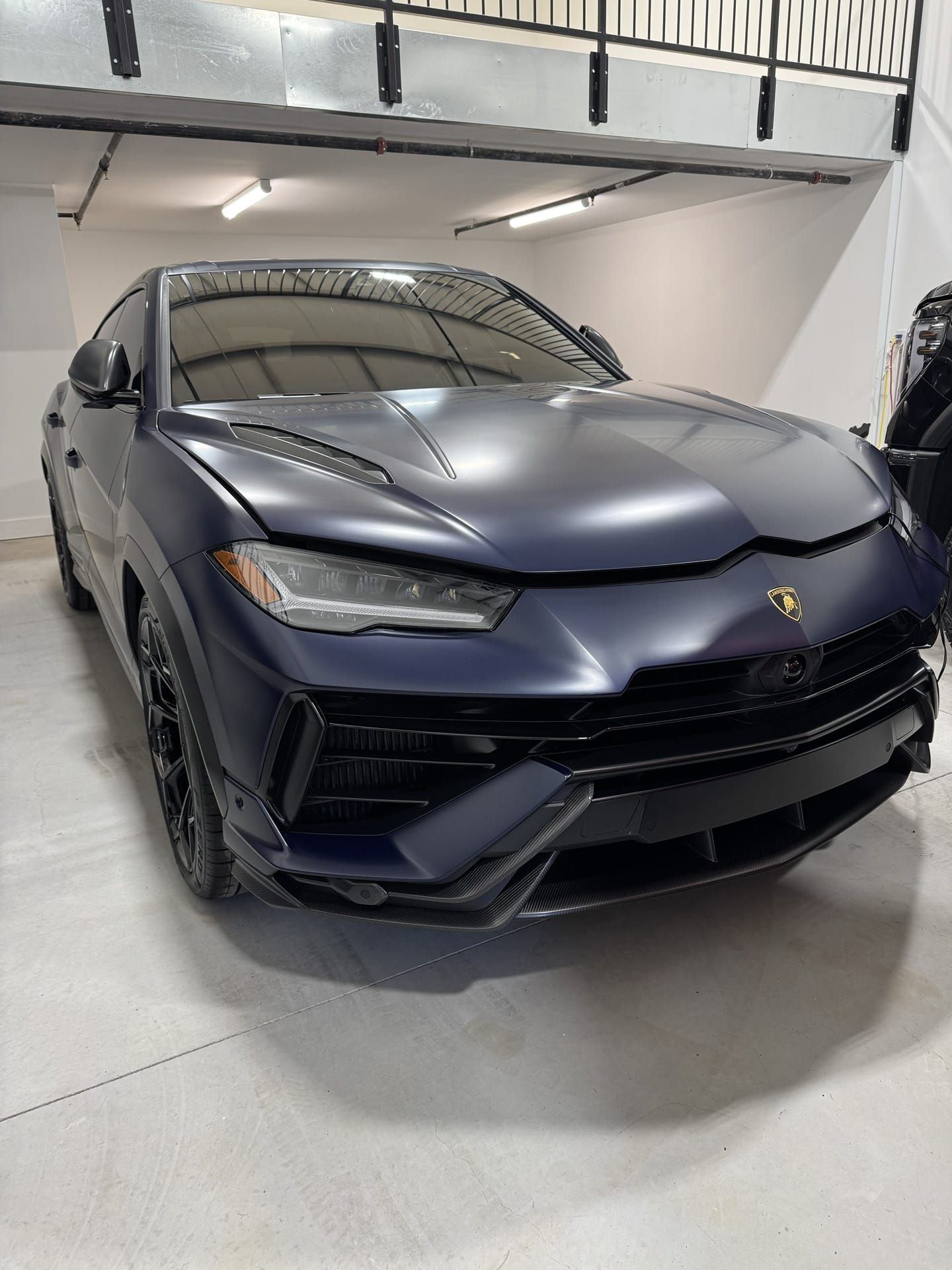 Blue Lamborghini Urus SUV in a garage, matte finish.