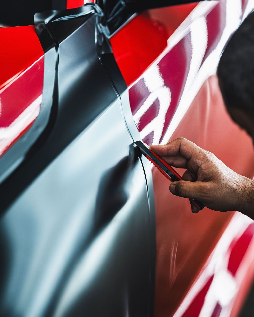 Person using a tool to smooth out black car wrap over a red vehicle.