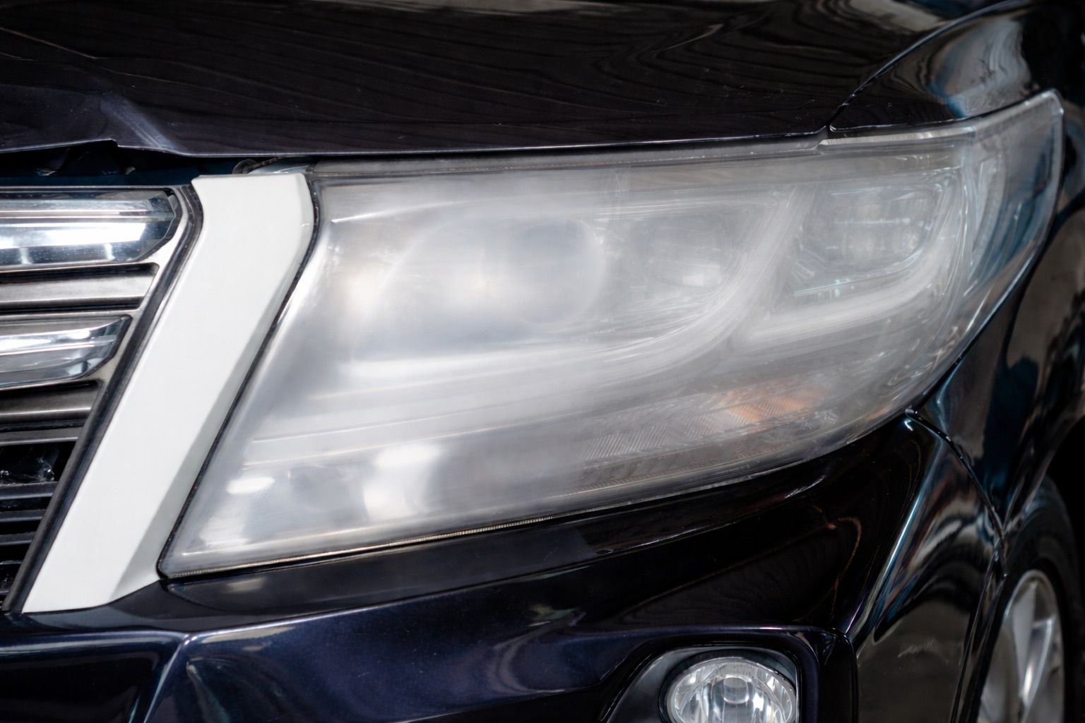 Cloudy headlight on a black vehicle, close-up shot.
