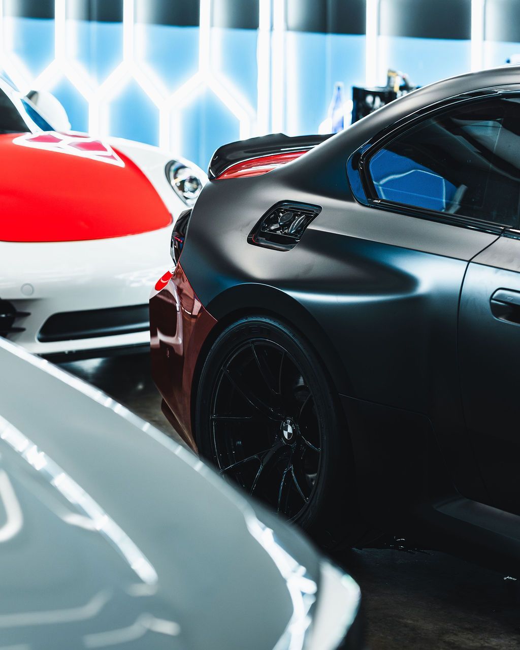 A group of luxury cars in a showroom, including a black coupe and a white sports car with a red hood.