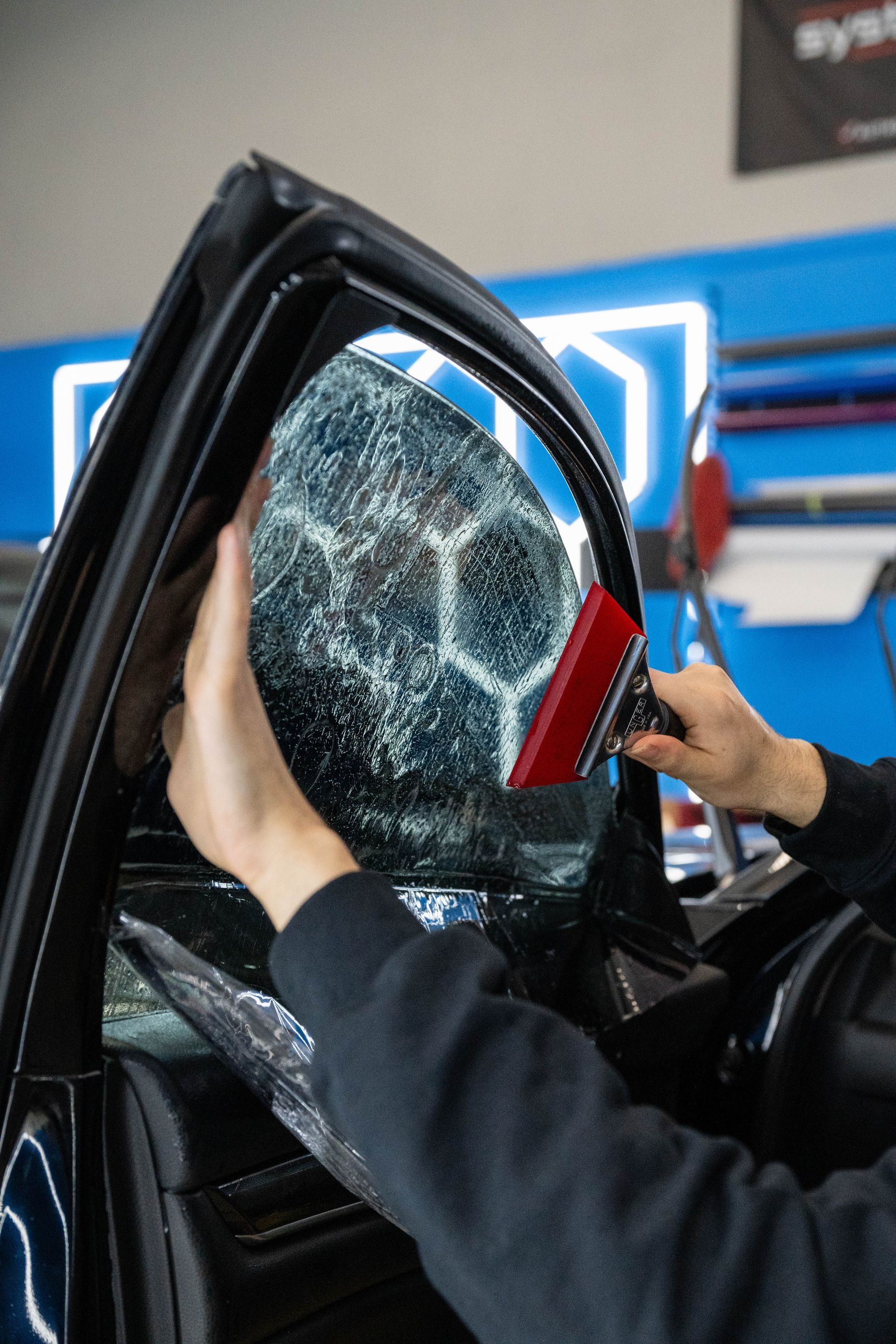 Person installing window tint on a car. The tint film has a honeycomb pattern, red squeegee tool used.