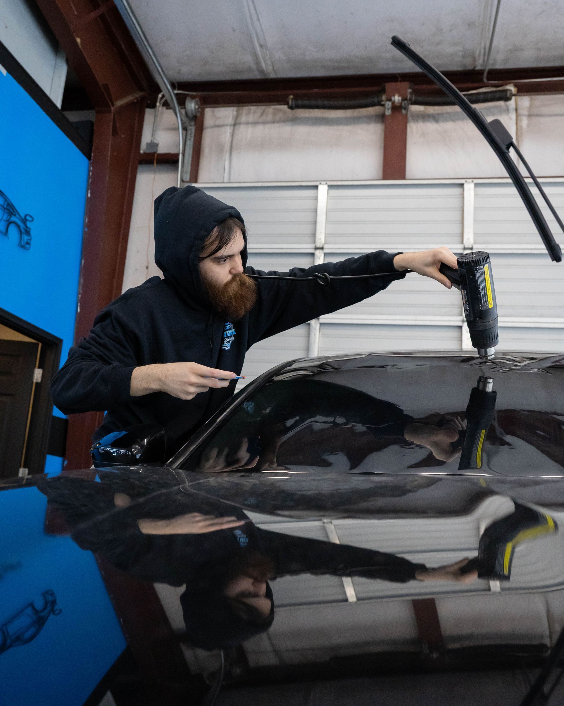 A person in a hooded sweatshirt using a tool on a car windshield.