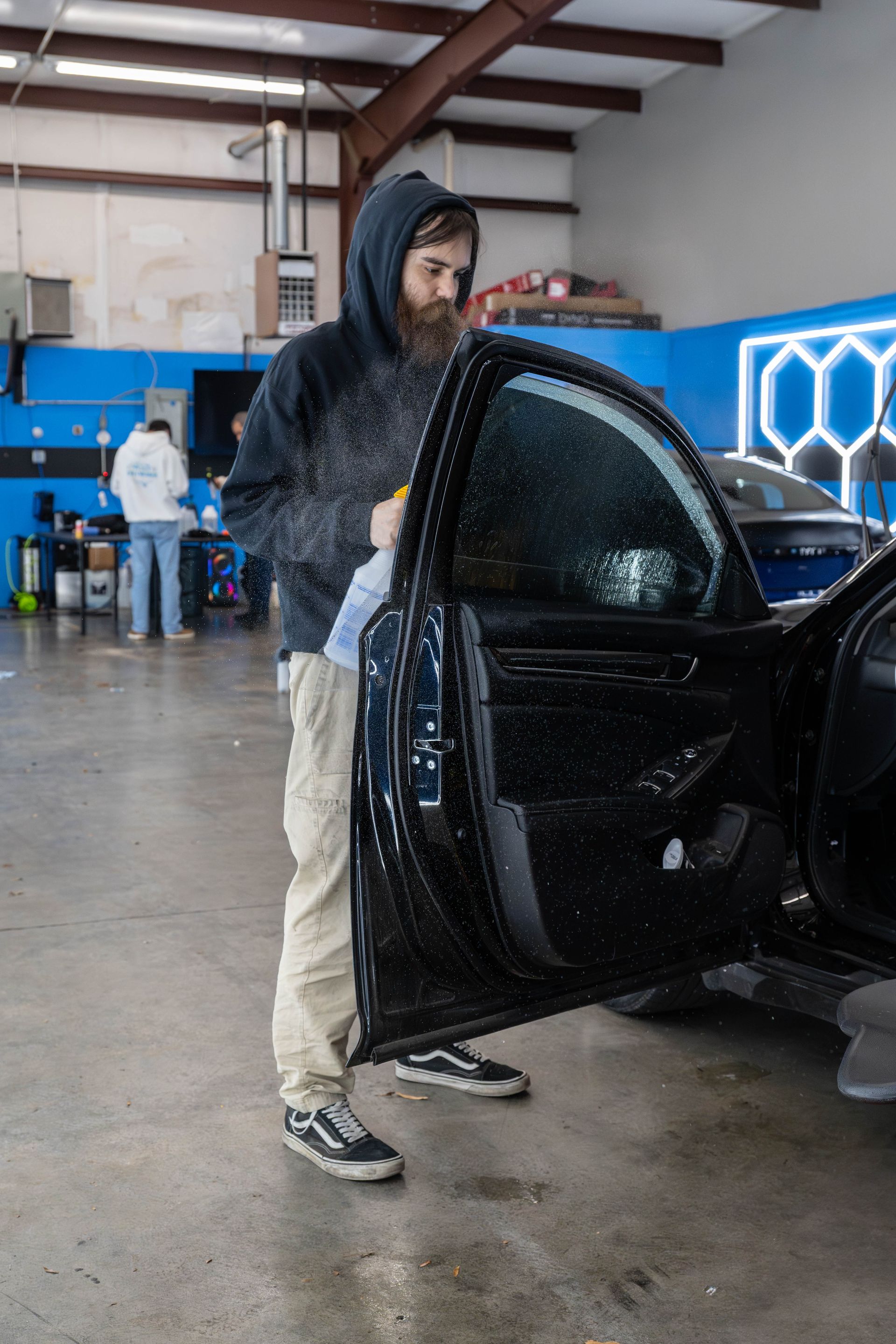 Man spraying car window with a bottle in a shop, concrete floor.