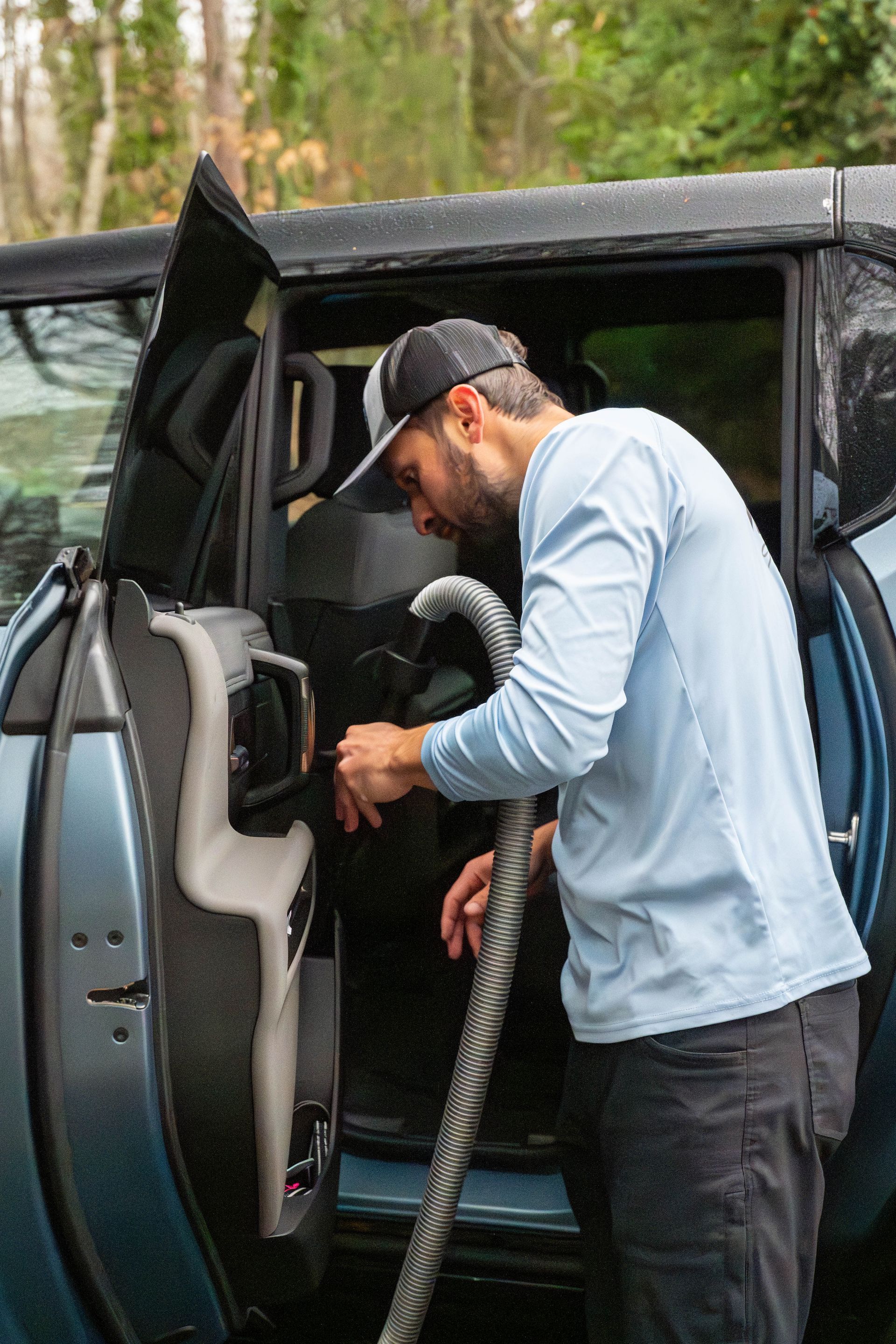 Man vacuuming the interior of a blue car with an open door.