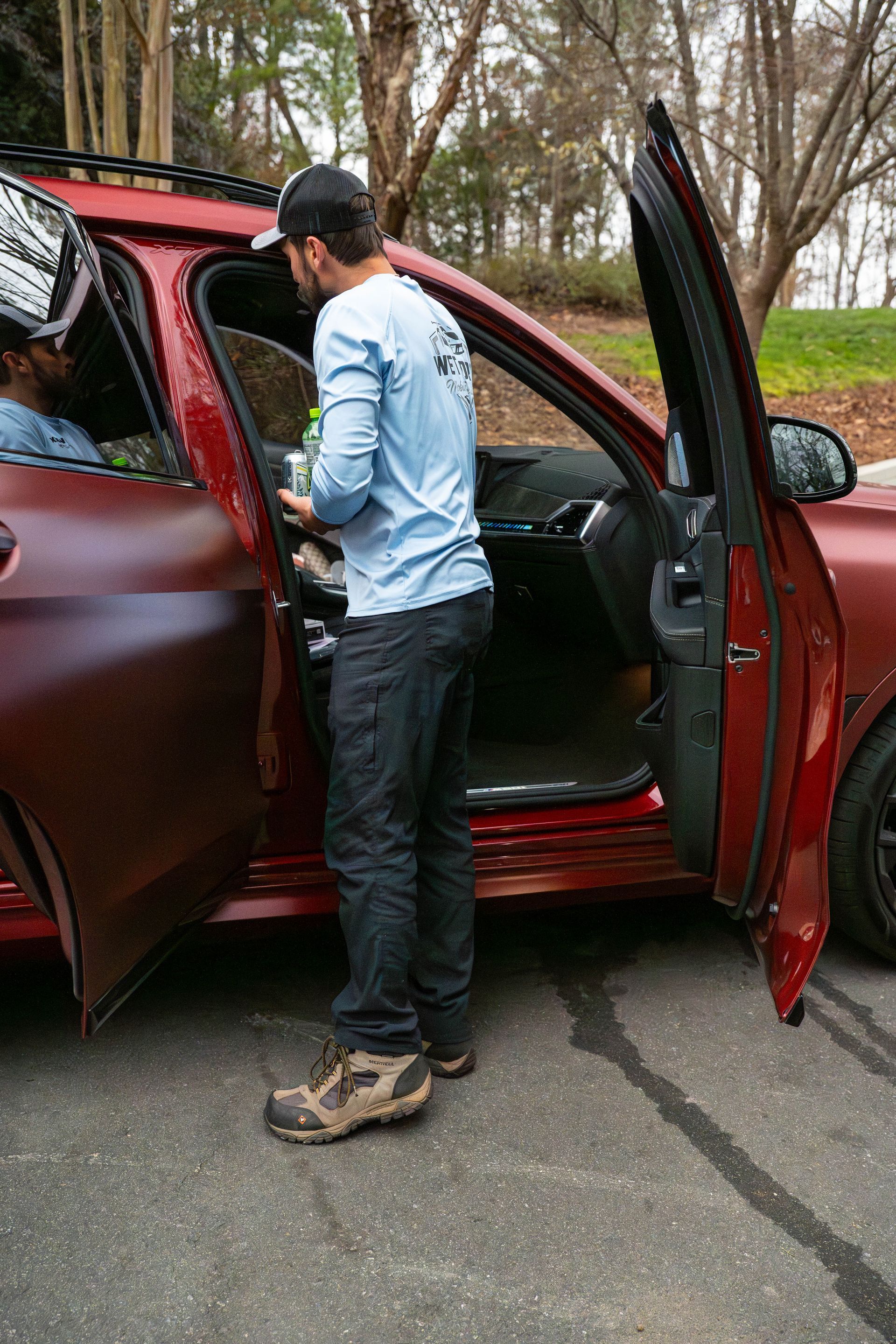 Man standing by open car door, holding a can. Red SUV parked on asphalt.