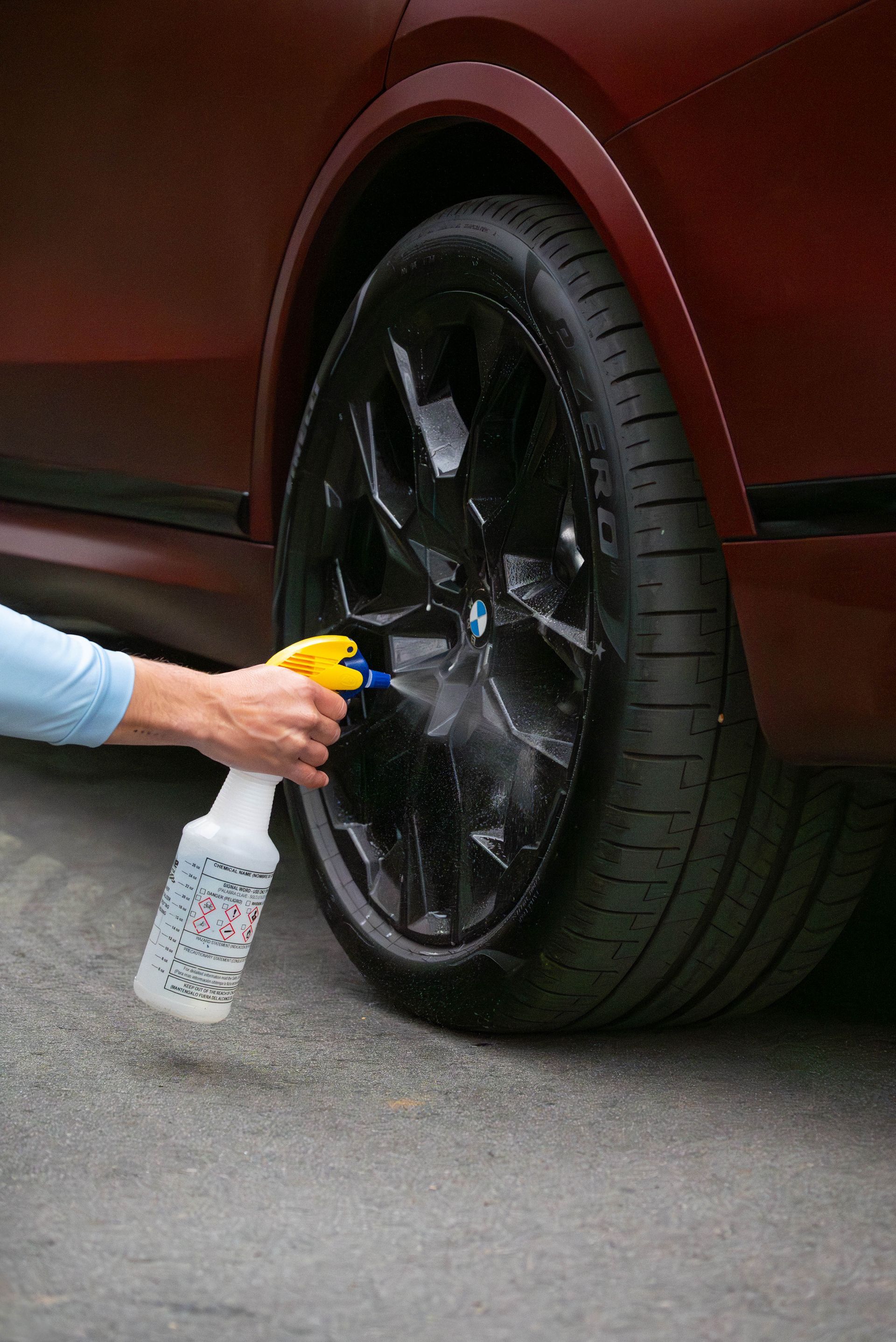 Person spraying black car wheel with a cleaning solution.