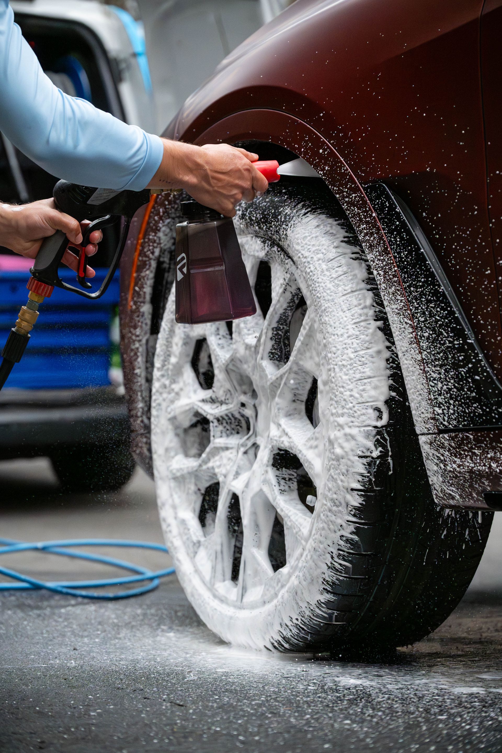 Person spraying soapy foam on a car tire and wheel at a car wash.