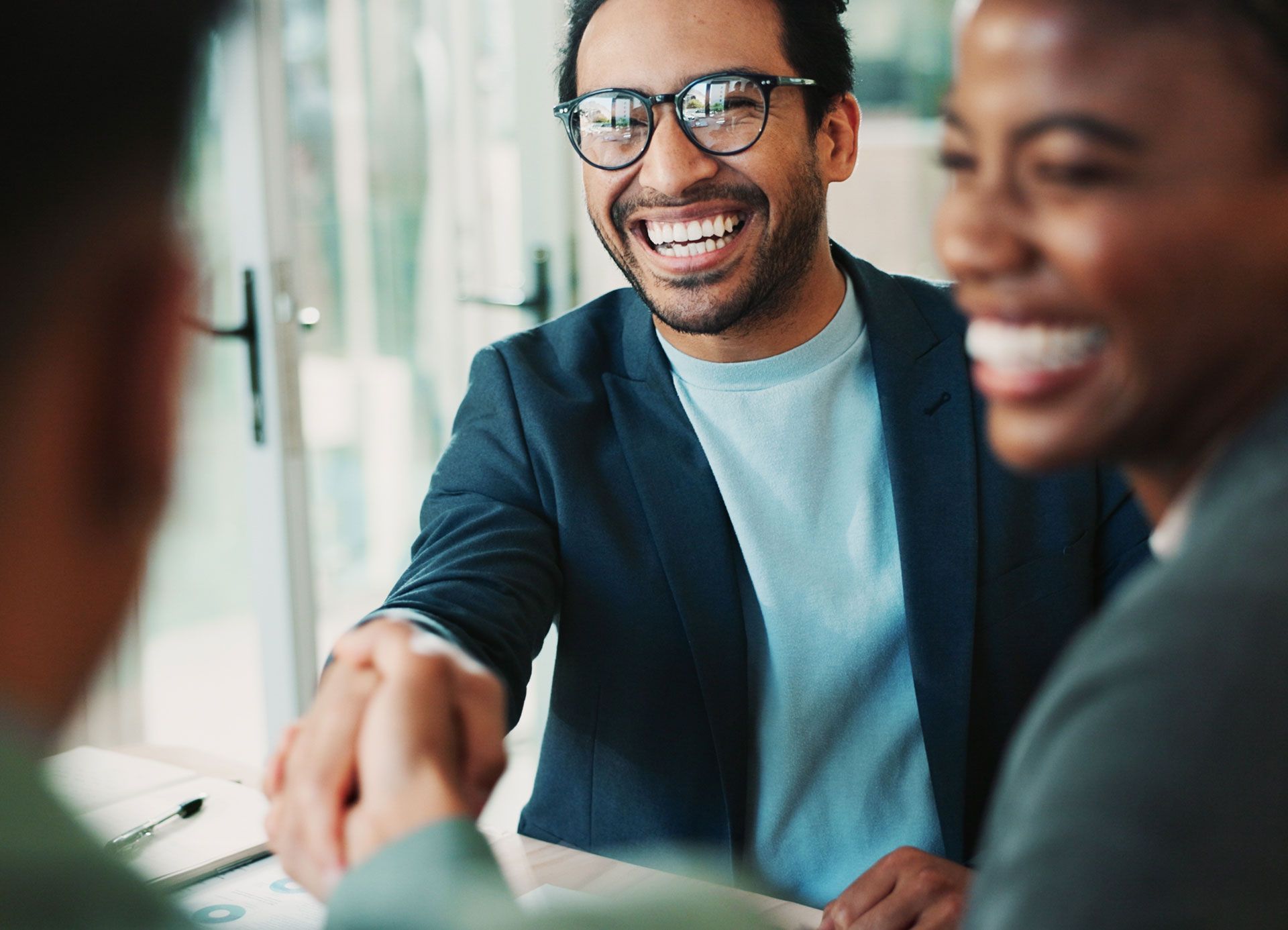 Man in glasses shakes hands with a person, smiling. Another person watches. In an office.