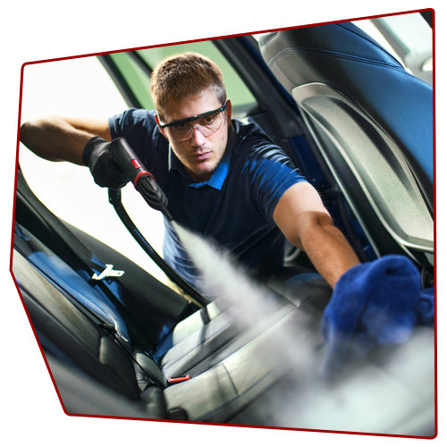 Person steam cleans car seat, wearing safety glasses and gloves, with a blue cloth in hand.
