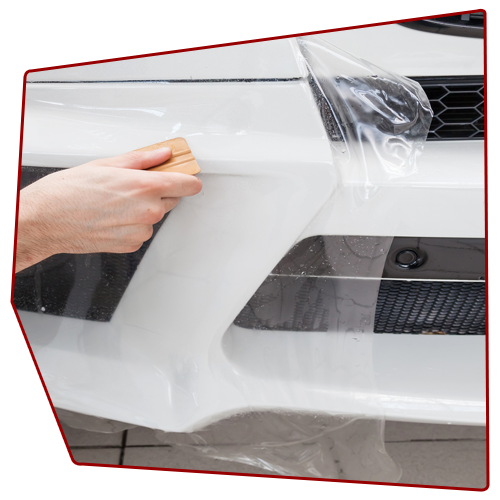 Person applying protective film to a white car bumper with a squeegee.