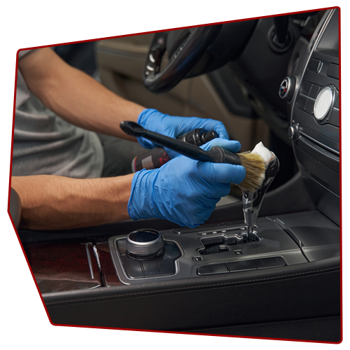 Person wearing blue gloves cleans a car's interior with a brush and cleaning solution.