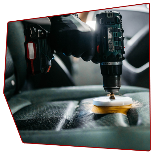 Person using a drill with a scrubbing brush on a car seat.