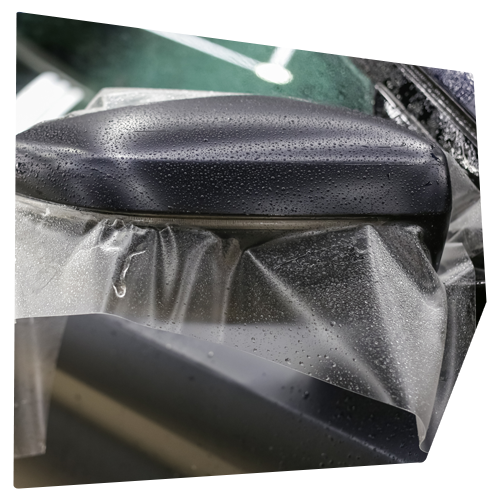 Black object covered in clear plastic with water droplets, angled view.