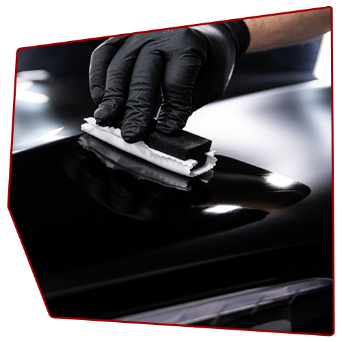 Black-gloved hand applying ceramic coating to a shiny black car surface with applicator pad.