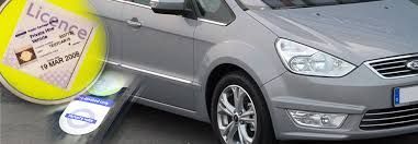 A silver car is parked next to a yellow sign that says licence.