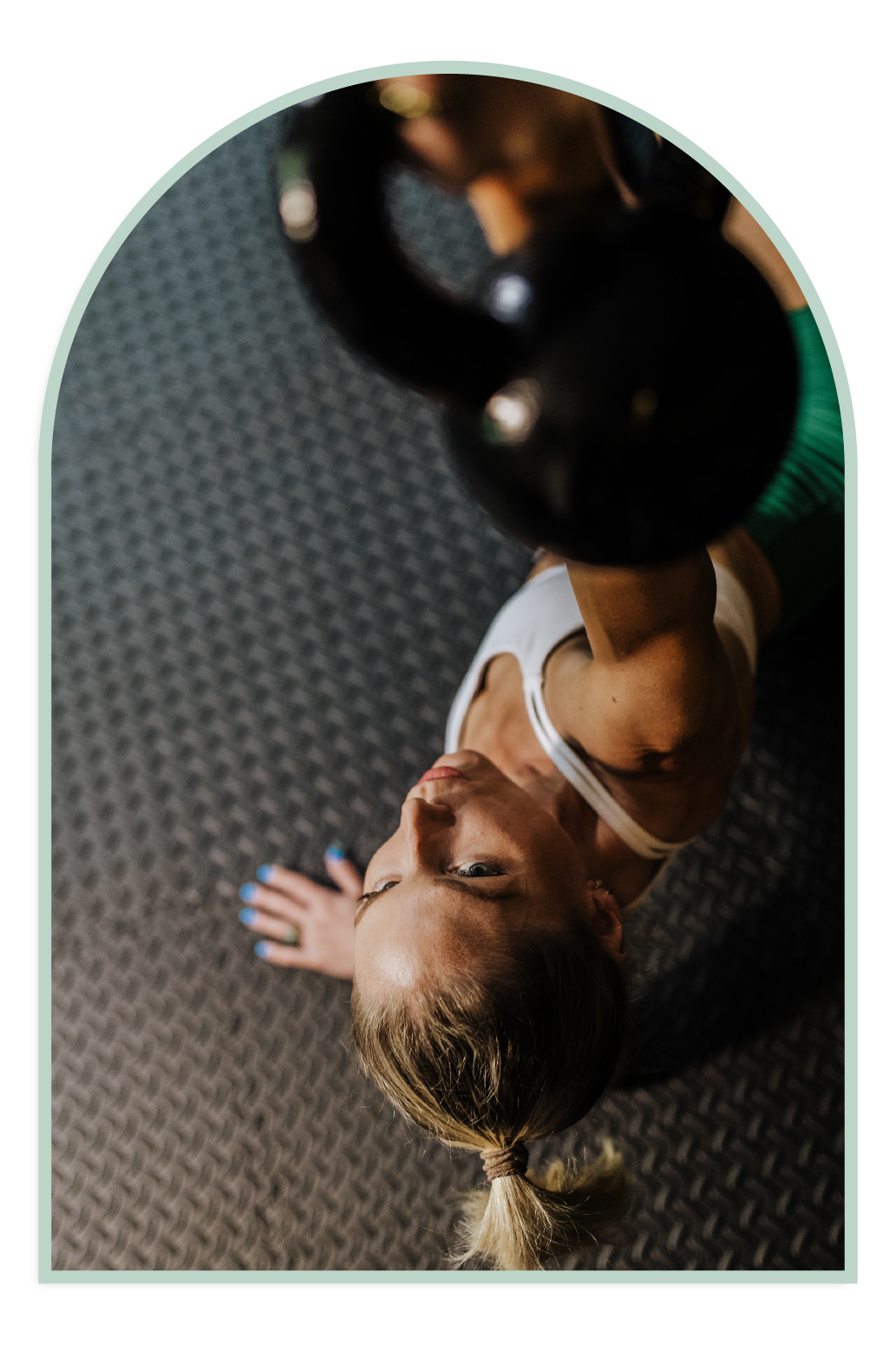 Woman doing kettlebell workout, white tank top, green leggings, gym setting.