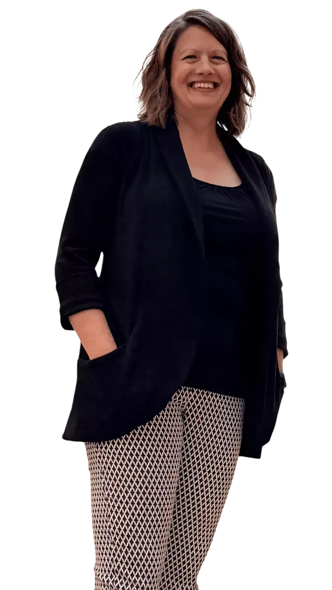 Woman smiling, wearing a black jacket over a black top and patterned pants, hands in pockets.