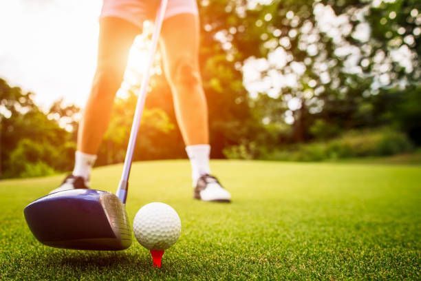 Golfer addressing a golf ball on a green fairway at sunset