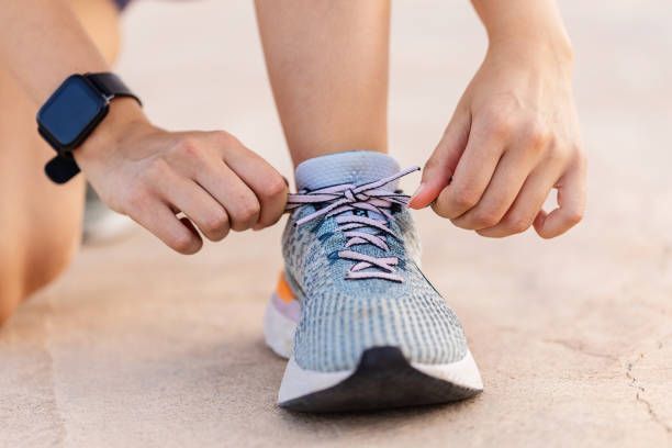Hands tying the laces of a blue running shoe on a concrete surface