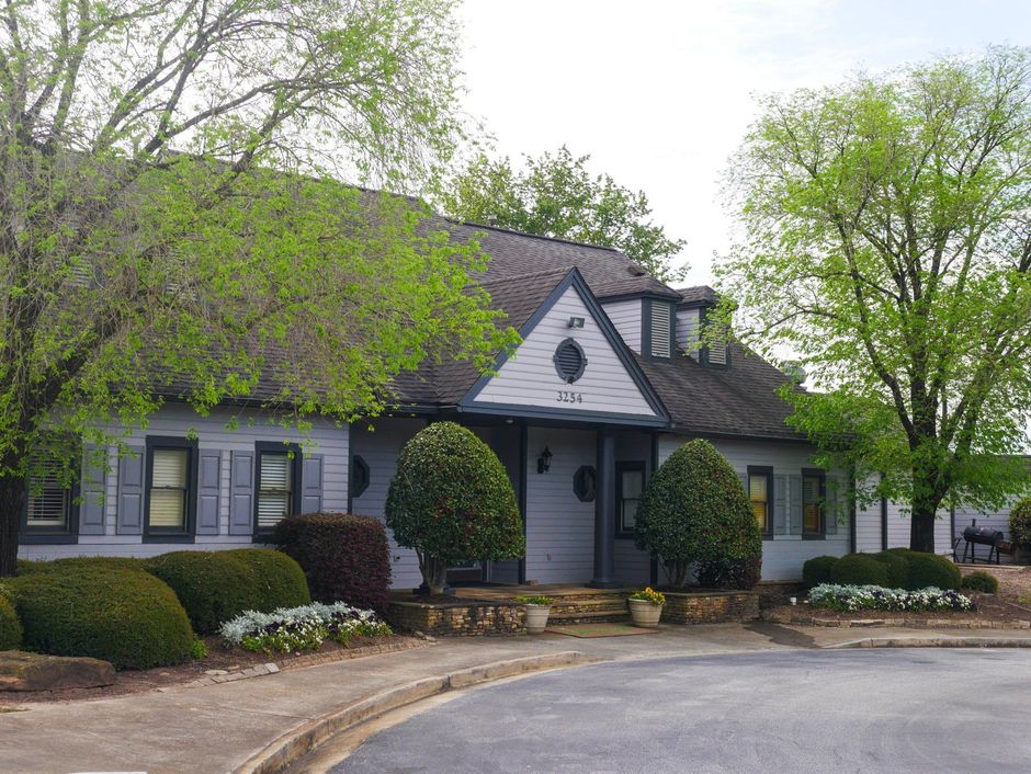 A white house with a triangle roof is surrounded by trees and bushes.