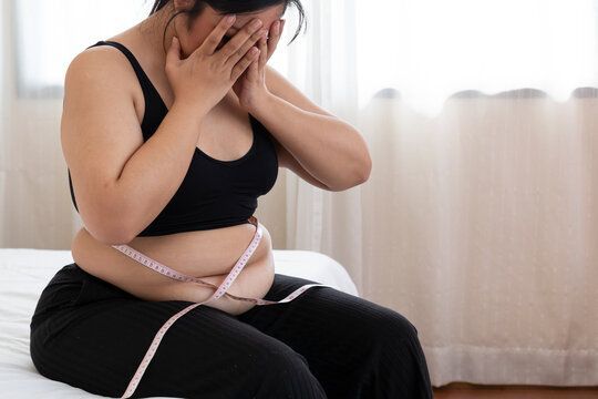 A woman is sitting on a bed with a measuring tape around her waist.